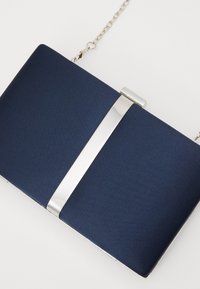Granatowa kopertówka o gładkiej fakturze, ze srebrnym metalowym zapięciem i akcentem oraz odpinanym łańcuszkiem. Prostokątny kształt.
