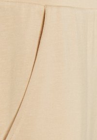 Tecido bege com uma textura suave, apresentando um bolso lateral e um detalhe de costura subtil para um design descontraído.