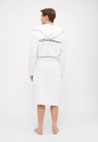 Accappatoio bianco in spugna con cappuccio, cintura e ricamo "EA7 Emporio Armani" sul retro. Tessuto morbido, design fino al ginocchio.