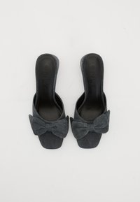 Mules in denim aperti con suola piatta. Presentano un grande fiocco decorativo sulla parte anteriore. Colore: blu denim scuro con una superficie liscia.