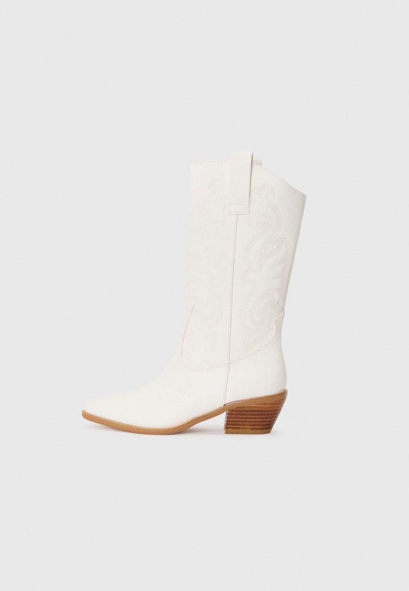 Bottes blanches de style western à chevilles avec un bout pointu, un tissu texturé, un design brodé et un talon en bois empilé.