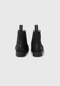 Fekete bőr bokacsizmák rugalmas oldalsó panelekkel, hátul húzófülekkel és masszív gumi talppal. Simább felület és áramvonalas sziluett.