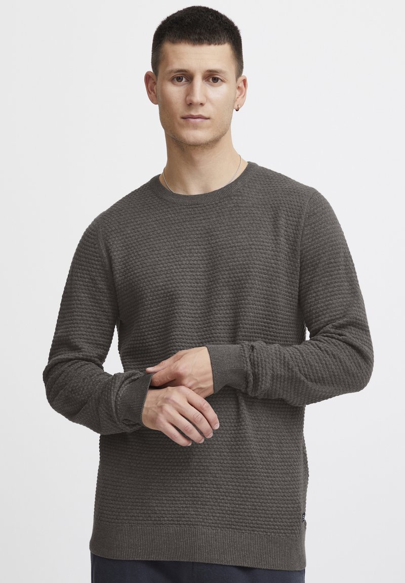 Maglione grigio scuro con texture, collezione girocollo e maniche lunghe. Presenta polsini e orlo a costine, evidenziando il motivo tessuto.
