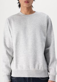 Sweat-shirt gris en tissu mélange de coton, avec un col rond, des poignets et un ourlet côtelés, présentant une texture lisse et un design simple.