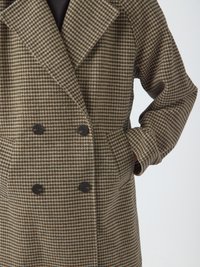 Cappotto doppiamente abbottonato realizzato in tessuto houndstooth testurizzato marrone e crema, caratterizzato da grandi bottoni scuri e tasche laterali.