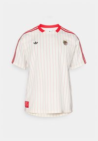 Bílé tričko s krátkým rukávem s červenými vertikálními pruhy, červeným límcem a třemi červenými pruhy na rameni. Obsahuje vyšívané logo a detailní štítek.