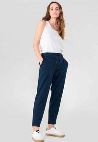 Pantalones jogger azul marino con cintura ajustable, bolsillos laterales, diseño de pierna ajustada, combinados con una camiseta sin mangas blanca y zapatillas blancas.
