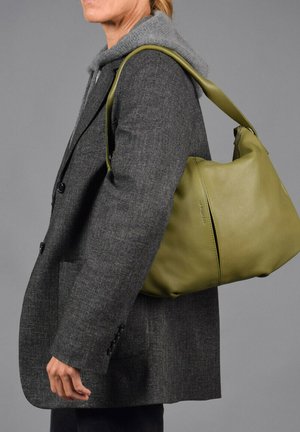 Hobo tas van olijfgroen leer met een slouchy vorm, featuring een zachte textuur en een enkele schouderband, gedragen met een grijze blazer.