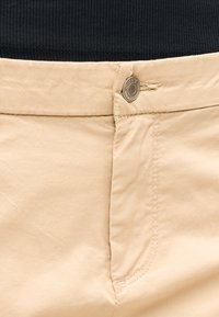 Ceinture de pantalon beige avec un bouton métallique marqué "ONLY", associée à un t-shirt noir côtelé rentré à l'intérieur.