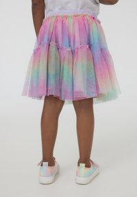 Gonna in tulle a più strati nei colori arcobaleno pastello, con dettagli scintillanti e fascia elastica in vita, abbinata a sneakers bianche.