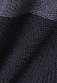 Tela texturizada de azul marino oscuro con un patrón de punto fino, mostrando una superficie lisa y un ligero brillo, que cae suavemente en pliegues.