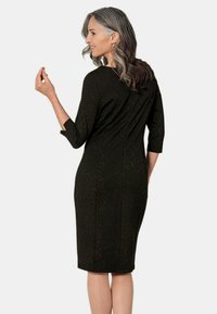 Schwarzes Kleid mit subtilen goldenen Pünktchen, figurbetonte Silhouette, Dreiviertelärmel, knielang und Rückennahtdetails.