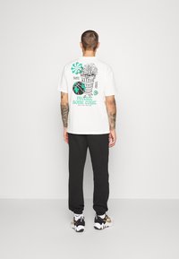 Vit bomull t-shirt med en grafisk design som visar en växtbädd och text, parat med svarta sweatpants och sportiga skor.