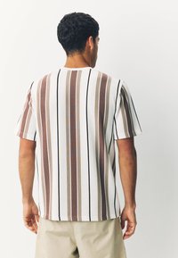 Striped short-sleeve shirt in white, featuring vertical lines in brown, beige, and black. Ribbed texture with a relaxed fit.