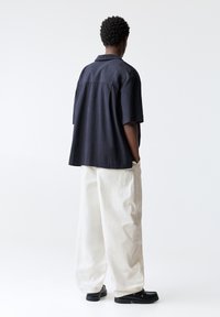 Short-sleeve navy shirt with a textured design, paired with loose white trousers and black shoes, viewed from the back.