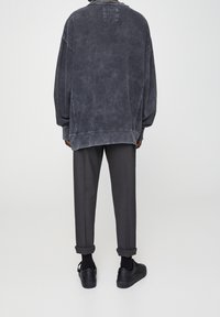 Sudadera de gran tamaño en gris oscuro con una textura desgastada, combinada con pantalones grises ajustados y zapatillas negras, con puños enrollados.