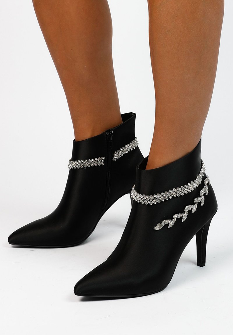 Zwarte satijnen enkellaarsjes met puntige neuzen en stiletto hakken. Versierd met sprankelende strass-kettingen rond de enkel, met een rits aan de zijkant.