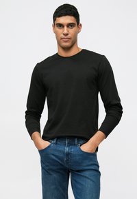 Mustapituinen pitkähihainen t-paita, jossa on pyöreä pääntie, yhdistettynä sinisiin farkkuihin. Kangas näyttää sileältä ja se on vartalonmyötäinen.