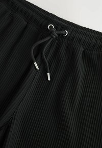 Shorts plissés noirs avec une taille élastique, dotés d'un cordon de serrage avec des embouts en argent. Tissu texturé, conception légère.