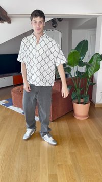 Kortærmet skjorte med et hvidt og sort diamantmønster, parret med grå baggy bukser og sølv sneakers, stående på et trægulv.