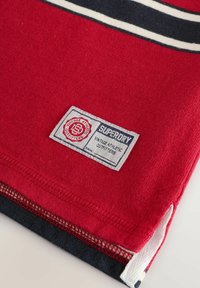 Punane puuvillane T-särk valgete ja tumesiniste triipudega, mille ääres on Superdry kaubamärgi silt ning tekstureeritud viimistlus.
