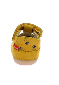 Sandalia infantil amarilla con textura suave de ante, correa de Velcro y detalles estampados en el talón, que incluye una etiqueta del logo de Kickers.