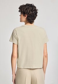 Beige, kortärmad T-shirt i mjuk bomull med rund halsringning. Baksidan är något kortare med en rak fåll och minimala sömnadsdetaljer.