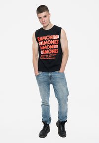 Black sleeveless t-shirt with red text reading "RAMONES LIVE," paired with light blue jeans and black lace-up boots. Plain background.