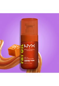 Pump bottle of NYX Fat Oil body oil in Caramel Mami scent with caramel swirl and caramel cube on purple background.