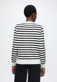 Maglione a righe bianco e nero con collo rotondo e maniche lunghe, caratterizzato da polsini e orlo a coste. Tessuto a maglia liscia.
