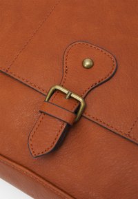 Brun læderrem med messingbeslag, der har en spids ende og syddede kanter, fastgjort til en matchende orange læderoverflade.