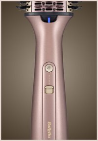 Handvat van een roségouden BaByliss haarstylborstel met aan/uit- en functietoetsen en een blauwe lichtindicator op een bruine achtergrond.