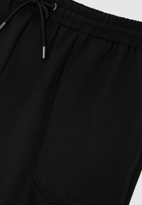 Mustad elastse vöökohaga püksid, esipõllega ja nöörsidemega, millel on hõbedased metallotsikud.