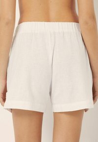 Pantalones cortos de lino blanco con cintura elástica, dobladillos enrollados y una textura suave. La vista trasera muestra su diseño holgado.