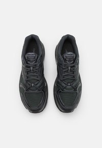 Svarta sportskor i mesh och syntetiska material, med rund tå, snörning och texturerade accenter på sidorna.