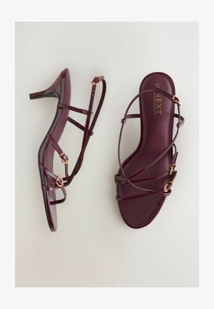 Sandales à talons en cuir verni bordeaux avec plusieurs lanières, accents en métal doré et un design épuré et minimaliste.