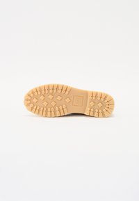 Sole of a shoe, featuring a light tan rubber material, ridged pattern for grip, and a logo embossed in the center with rounded edges.