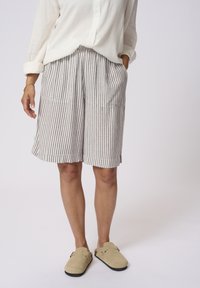 Striped shorts in light beige and dark brown, with a loose fit, elastic waistband, and front pockets. Paired with beige slip-on shoes.