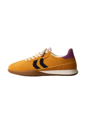 Baskets en daim jaune avec des rayures en chevron noires, des lacets crème, un insert violet au talon et une semelle en caoutchouc marron, vues de côté sur fond blanc.