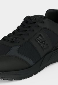 Μαύρο αθλητικό παπούτσι EA7 Emporio Armani με πάνελ από δίχτυ και δέρμα, κορδόνια και υφασμένη σόλα, εμφανίζεται σε κοντινό πλάνο από την μπροστινή πλευρά.