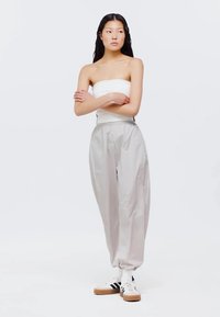 Svetlo šedé, voľné nohavice s elastickým pásom a zúženými manžetami, skombinované s bezramienkovým bielym topom a bielymi teniskami.