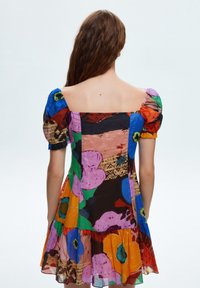 Robe colorée avec des manches ballon, décolleté carré, en tissu léger, ornée d'un motif floral dans des teintes de rose, bleu, vert et orange.