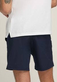 Pantalones cortos de color azul marino hechos de una tela suave con una cinturilla elástica. La camisa es de algodón blanco con una abertura en el dobladillo en los lados.
