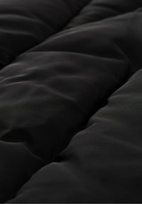 Tela acolchada negra con una textura suave, que presenta secciones elevadas y un leve brillo. El diseño enfatiza las costuras horizontales para añadir dimensión.