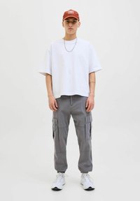 Weißes übergroßes T-Shirt, graue Cargohose mit Seitentaschen und weiße Turnschuhe. Rote Kappe mit Logodetail. Einfaches, lässiges Design.