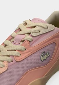 Ροζ και ροδακινί αθλητικό παπούτσι με υφασμάτινο επάνω μέρος με υφή, εκρού κορδόνια, λαστιχένια σόλα και ασημένιο λογότυπο κροκόδειλου στο πλάι.