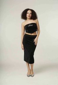 Črni žametni dvoodelni komplet, ki vključuje brezramni crop top z vezenjem "Juicy" in usklajeno midi krilo, dopolnjen s srebrnimi petami.
