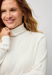 Biała sweterka z golfem, wykonana z miękkiego dzianiny, z długimi rękawami, z prążkowanym kołnierzem i mankietami, gładka struktura bez widocznych wzorów.