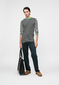 Svart og hvitstripete langermet skjorte med grønn krage, kombinert med mørke denimbukser og en svart tote-veske. Brune sko fullfører antrekket.