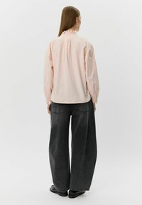 Svetloružová bavlnená blúzka s dlhými rukávmi, volánovým golierom a elastickými manžetami, v kombinácii s tmavosivými širokými nohavicami s vysokým pásom.